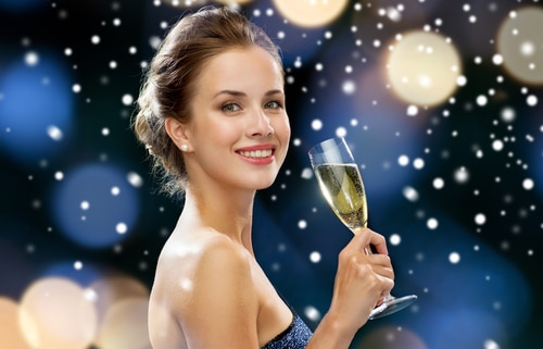 smiling woman in evening dress with glass of sparkling wine over night lights 500x321 1