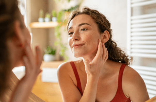 girl looking at mirror while touching her face and checking pimple wrinkles and bags under the eyes.