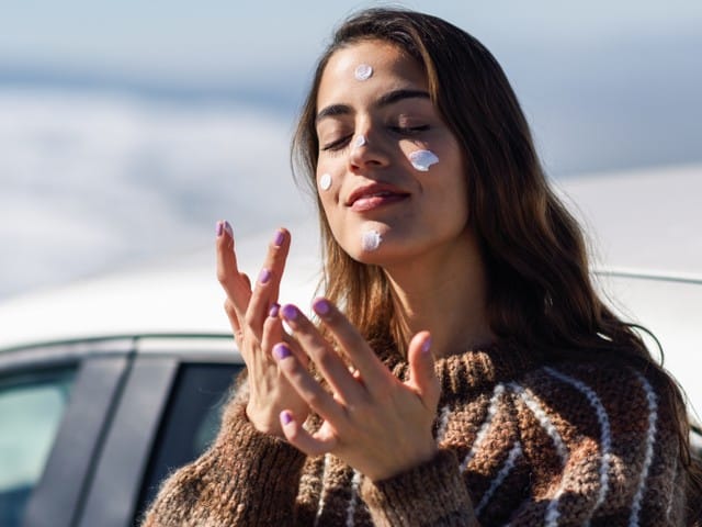 woman applying a sunscreen on her face in snowy mountains in winter