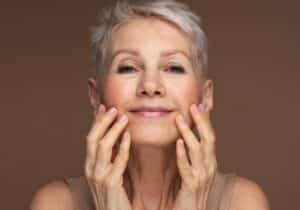 Portrait of gorgeous happy mature woman, senior older 60 year lady looking at camera touching her face