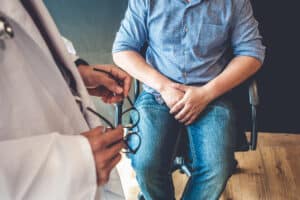 Man at doctor's office with hands over his groin area while discussing men's sexual health issues