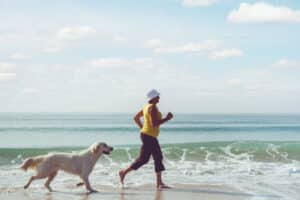 Woman holding hands around her midsection indicating a healthy gut Woman freely running on beach with dog
