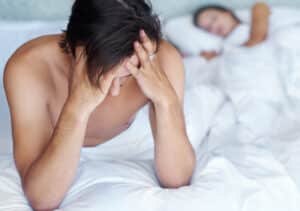 Woman holding hands around her midsection indicating a healthy gut Man sitting on a bed looking stressed about erectile dysfunction