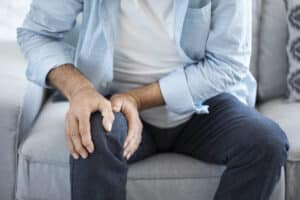 Woman holding hands around her midsection indicating a healthy gut Older man holding his knee due to orthopedic pain.